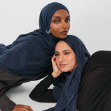 Two women wearing navy striped hijabs on a white background