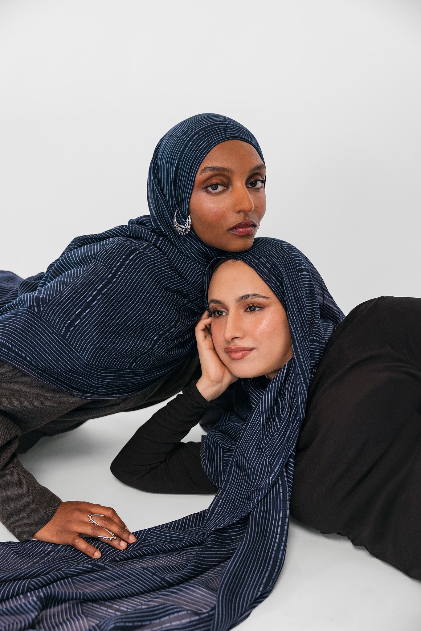 Two women wearing navy striped hijabs on a white background