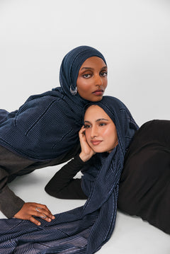 Two women wearing navy striped hijabs on a white background