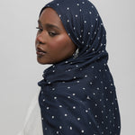 Woman wearing a navy hijab with white polka dots on a plain background