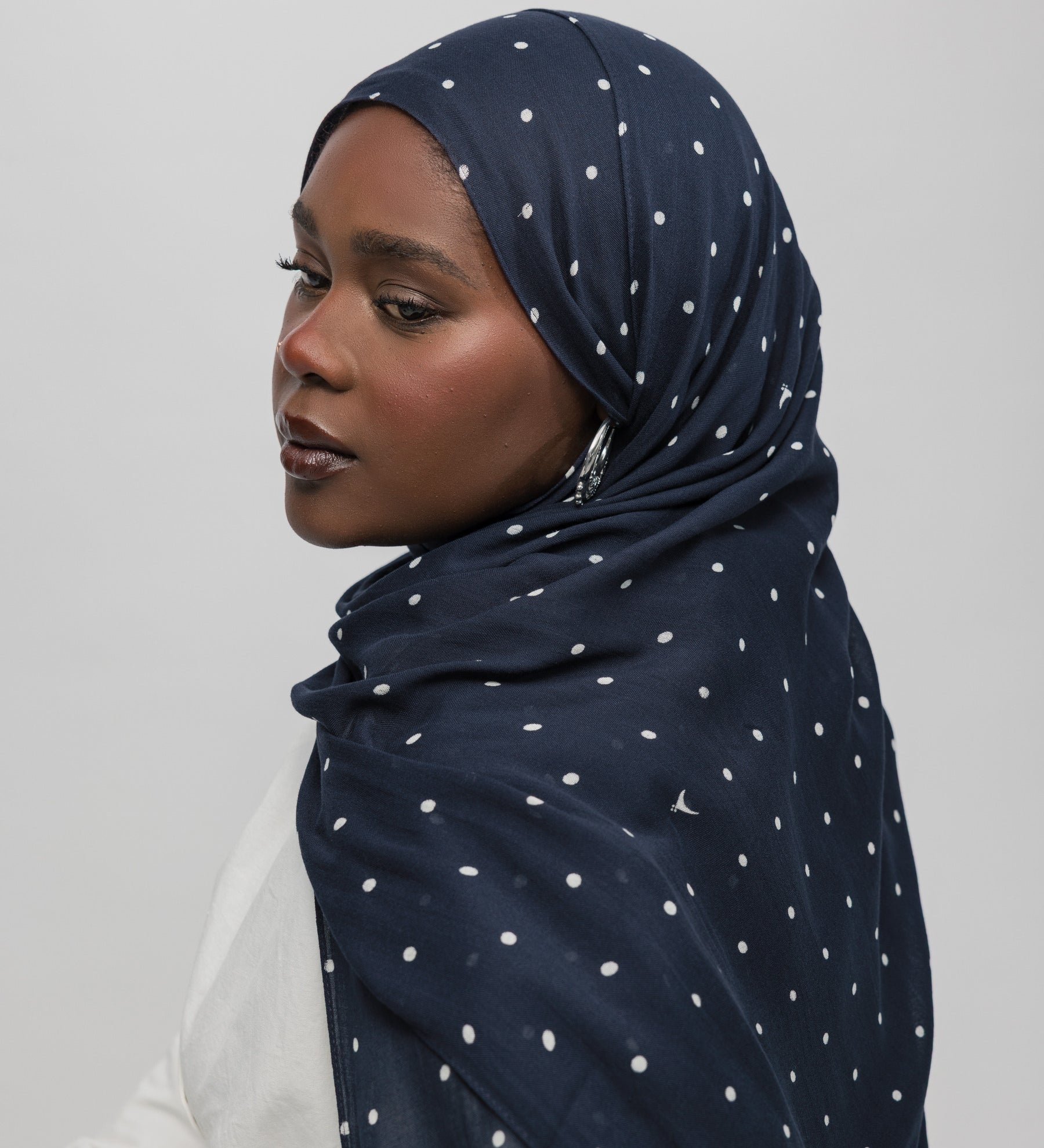 Woman wearing a navy hijab with white polka dots on a plain background