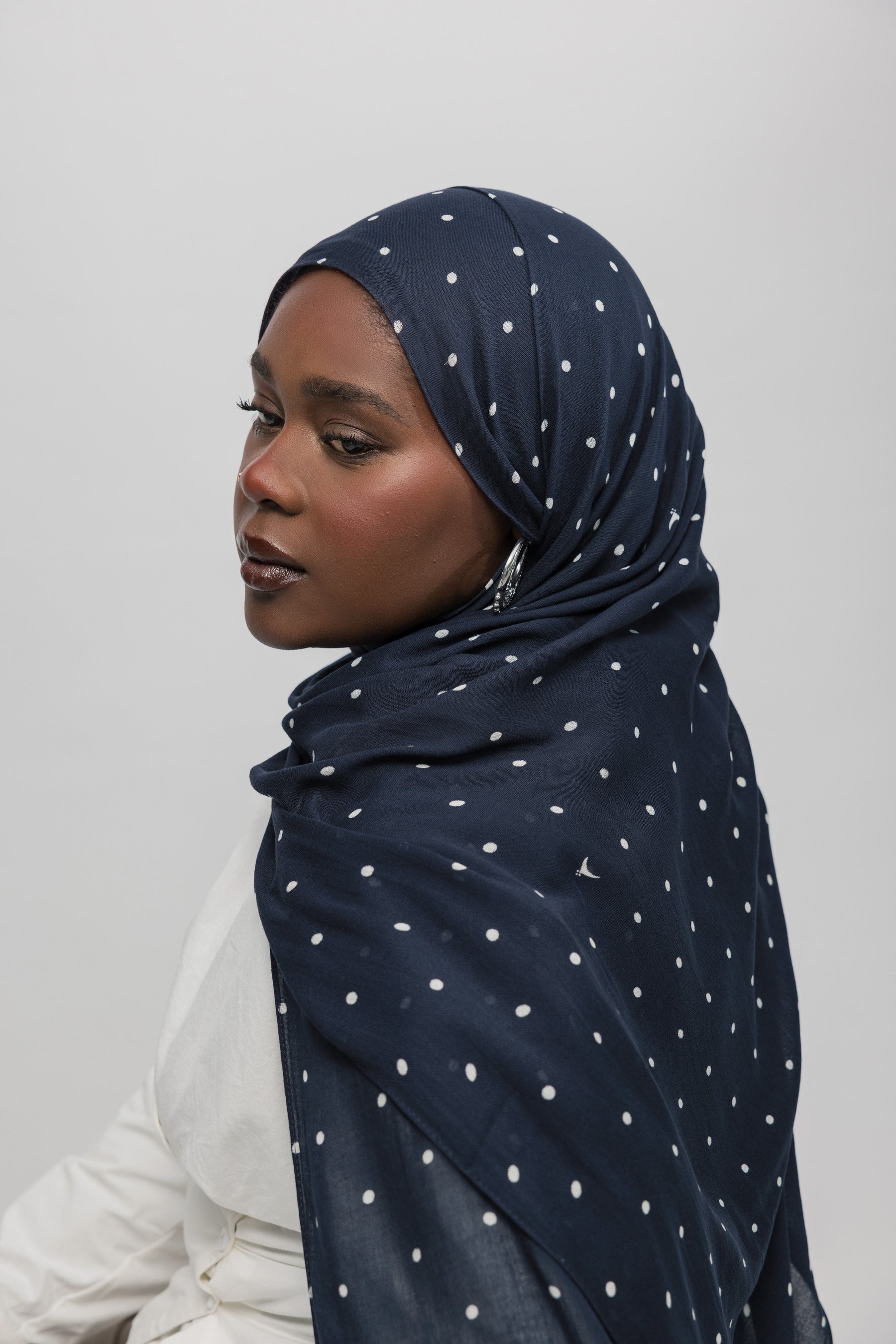 Woman wearing a navy hijab with white polka dots on a plain background
