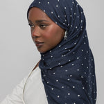 Woman wearing a navy hijab with white polka dots on a plain background