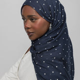 Woman wearing a navy hijab with white polka dots on a plain background