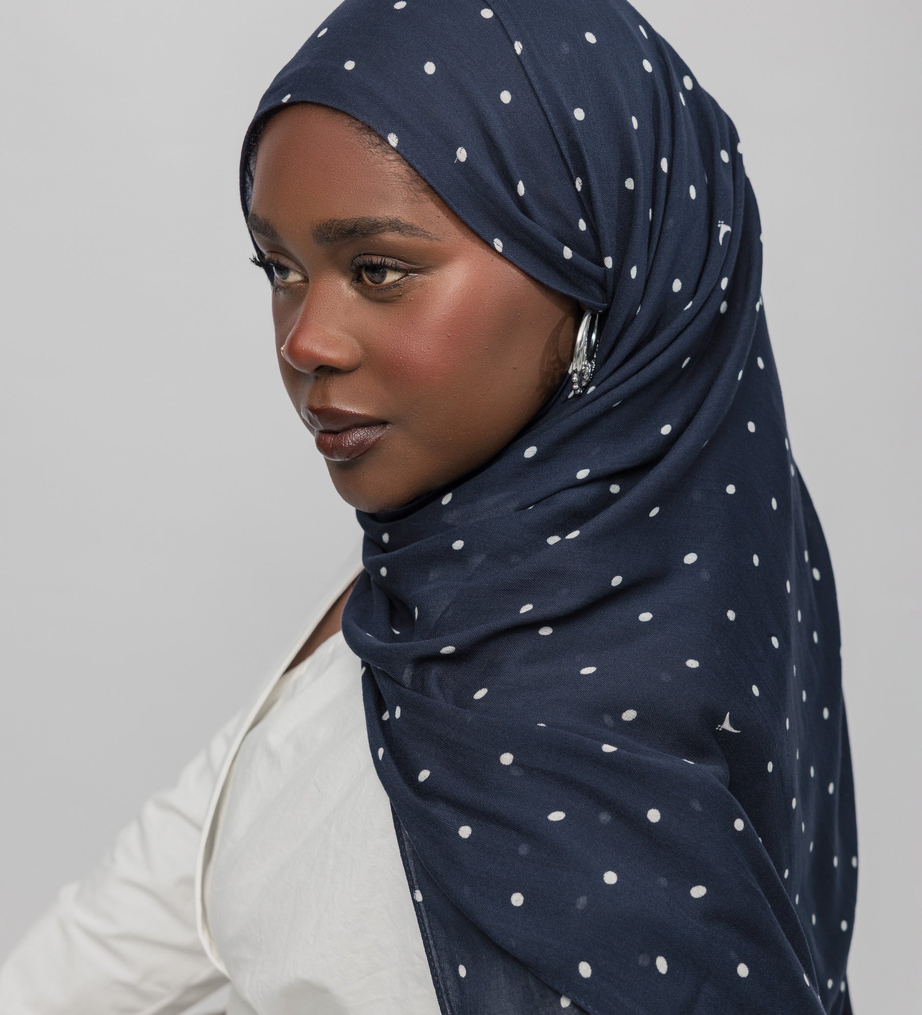 Woman wearing a navy hijab with white polka dots on a plain background
