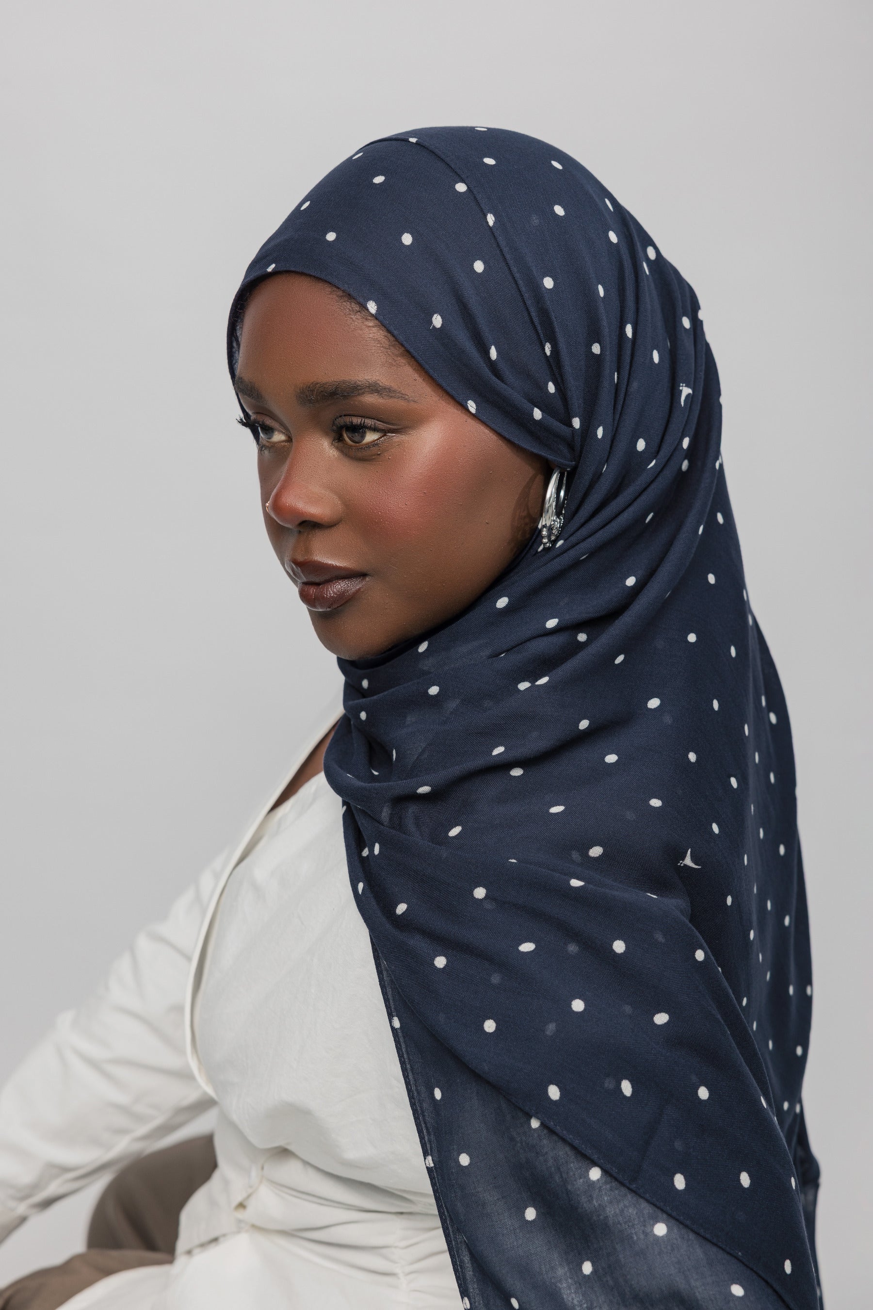 Woman wearing a navy hijab with white polka dots on a plain background