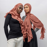 Two women modeling matching nectar ruffled hijabs and modest clothing against a plain light gray studio background.