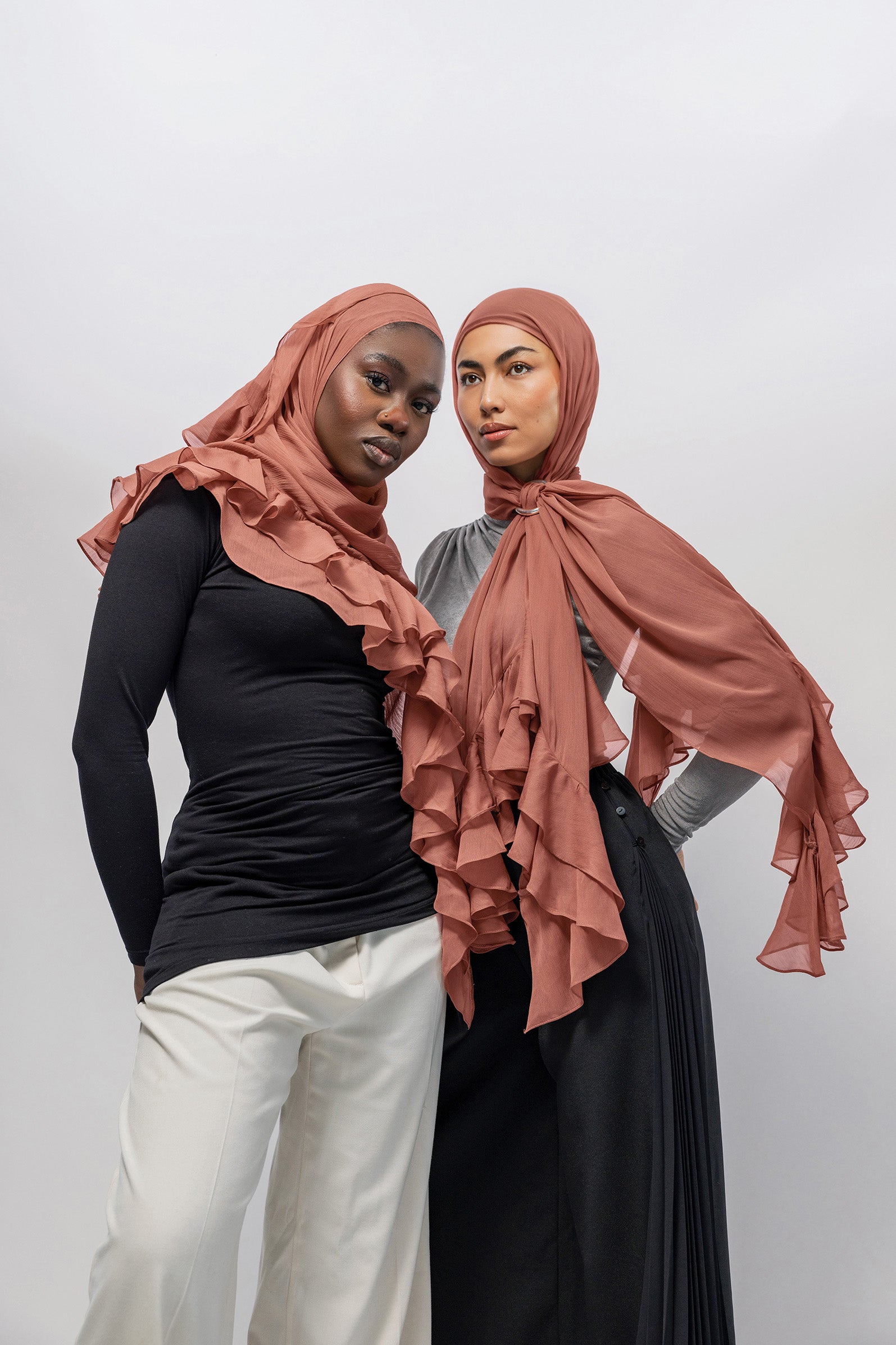 Two women modeling matching nectar ruffled hijabs and modest clothing against a plain light gray studio background.