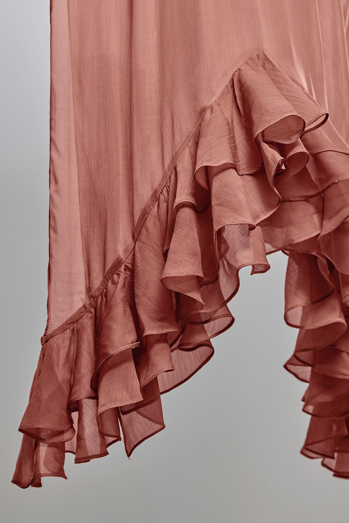 A close-up of a nectar pink ruffled fabric, showing the layered, cascading texture of the material against a neutral gray background.