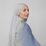 Woman wearing a light blue ombre hijab against a plain background