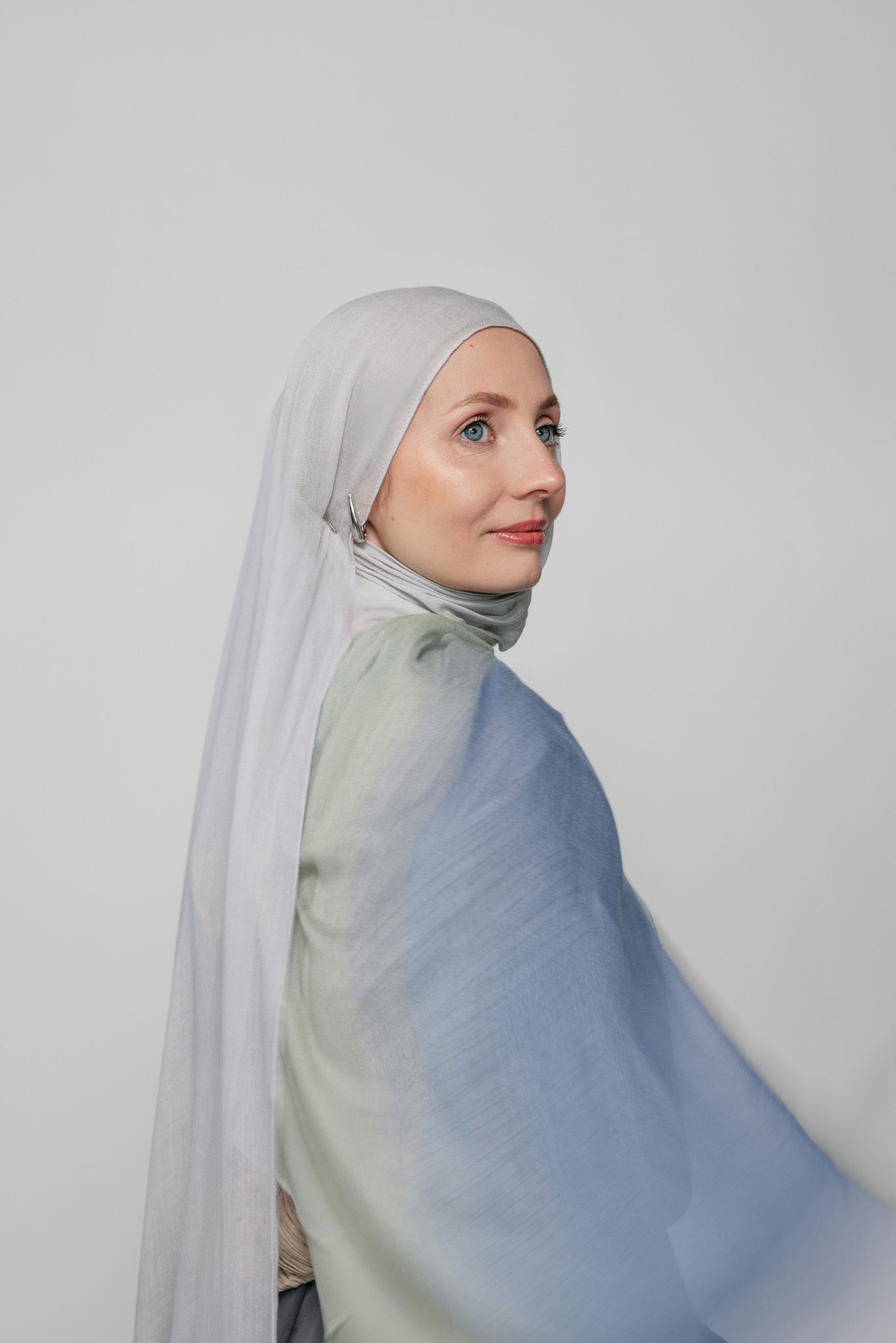 Woman wearing a light blue ombre hijab against a plain background