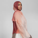 Woman wearing a brown and pink ombre hijab and white skirt on a plain background