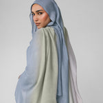 Woman wearing a light blue ombre hijab and beige outfit on a plain background