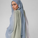 Woman wearing a light blue ombre hijab and beige outfit on a plain background