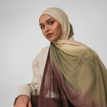 Woman wearing a beige and olive ombre hijab with a gradient effect on a plain background