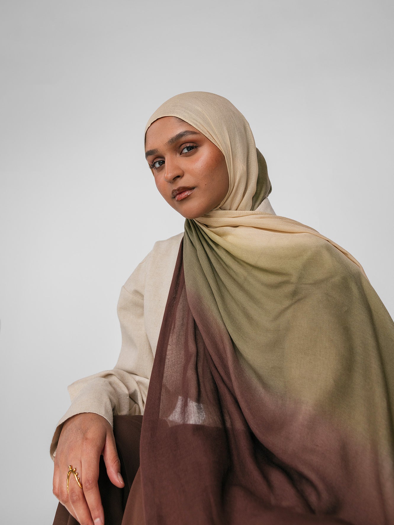 Woman wearing a beige and olive ombre hijab with a gradient effect on a plain background
