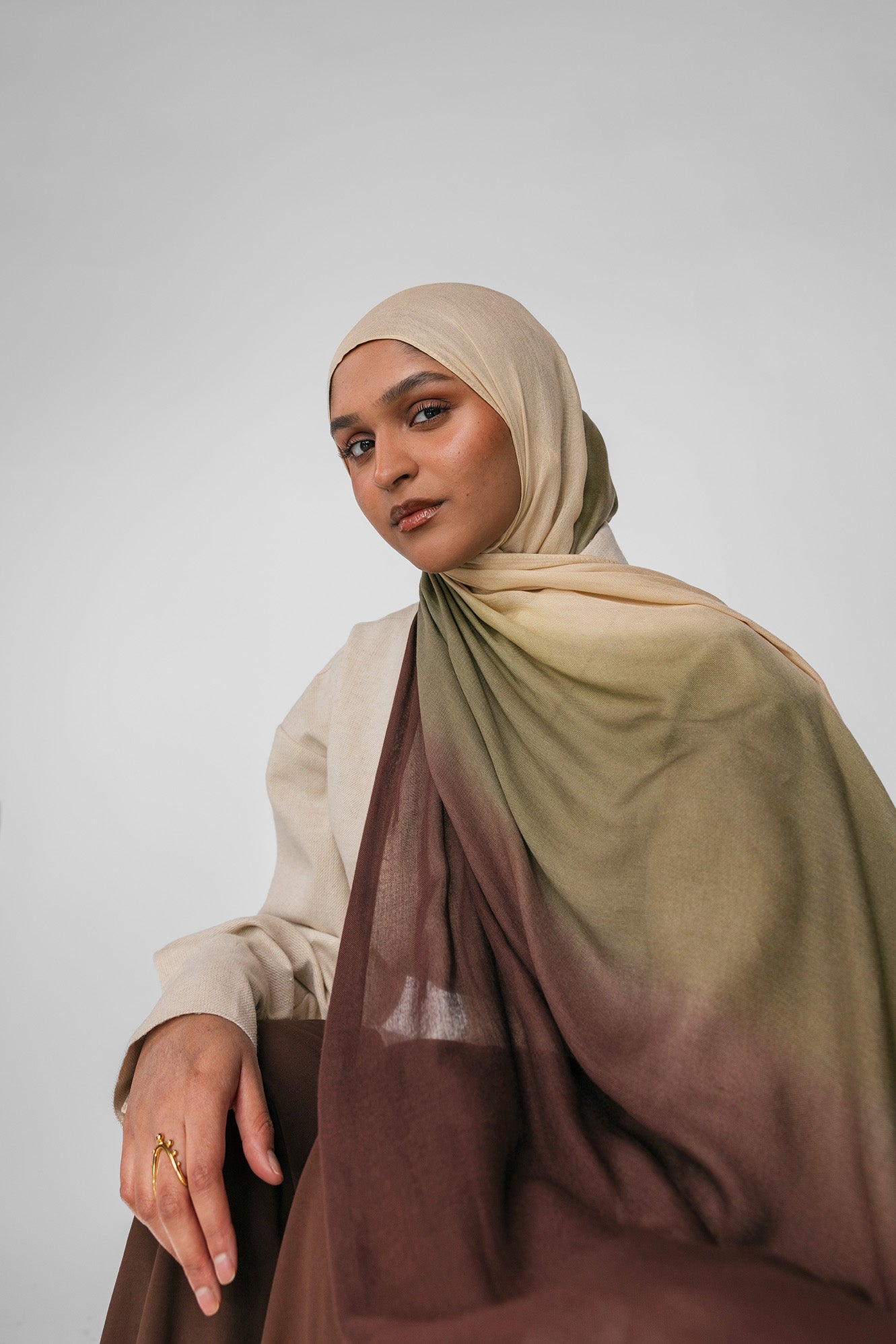 Woman wearing a beige and olive ombre hijab with a gradient effect on a plain background