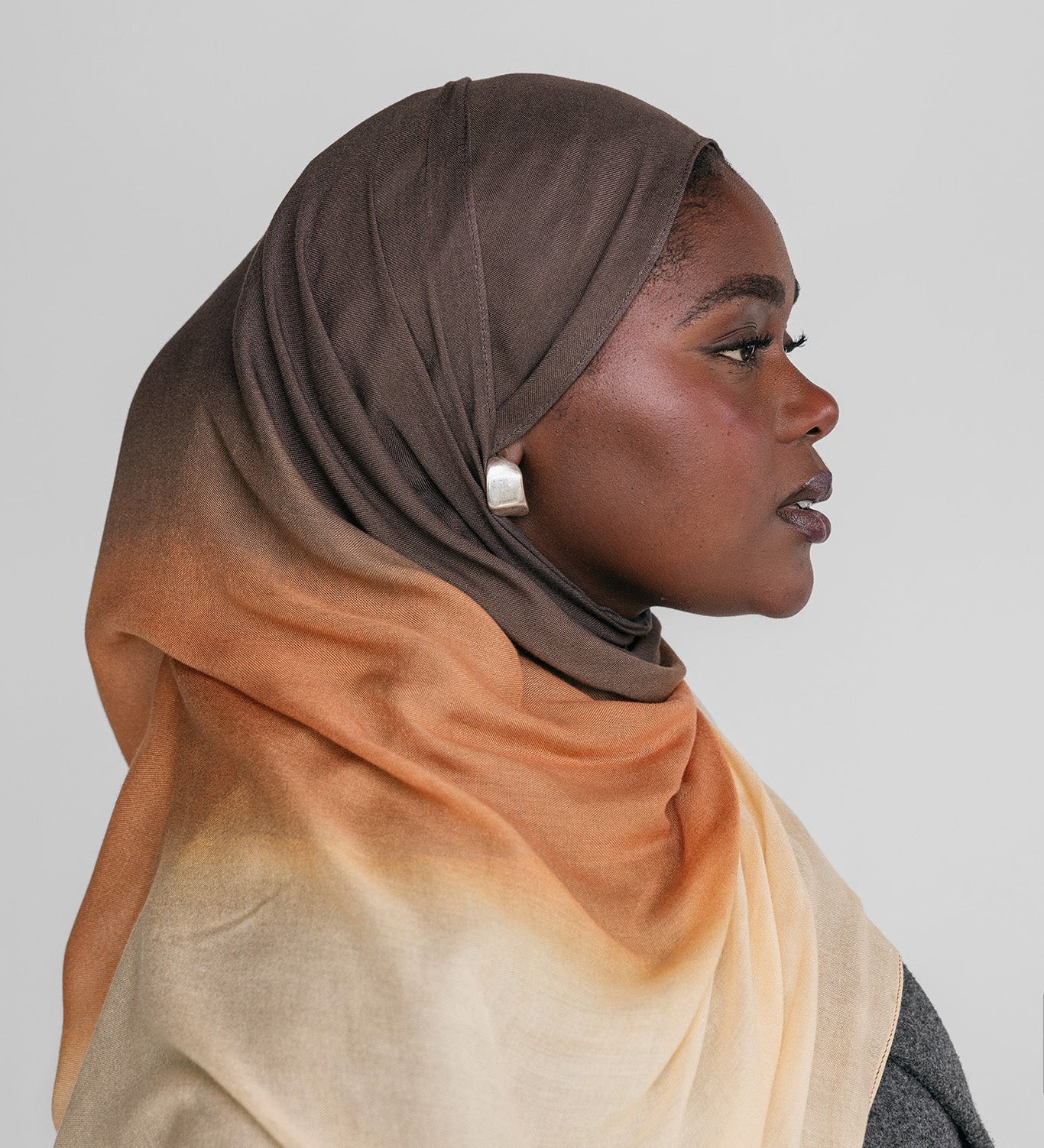 Woman wearing a ombre gradient hijab in brown, orange, and beige on a plain background