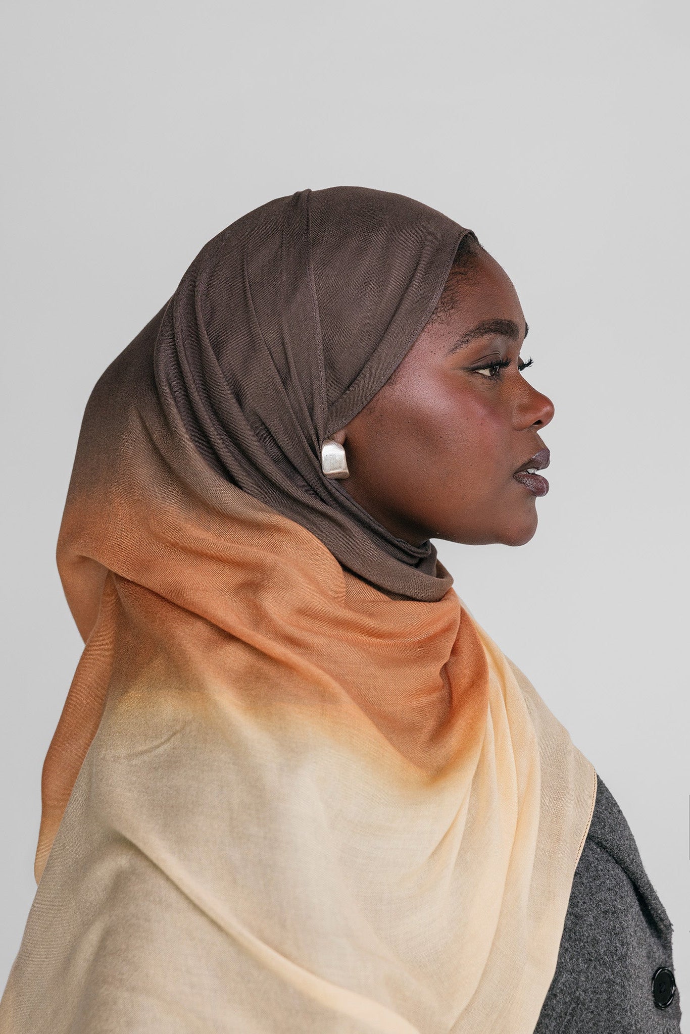 Woman wearing a ombre gradient hijab in brown, orange, and beige on a plain background