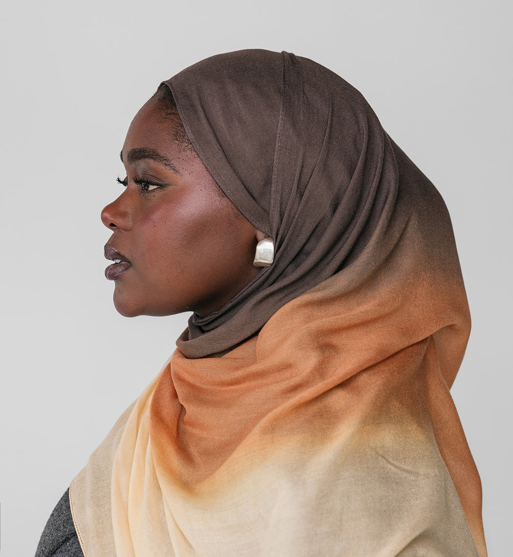 Woman wearing a gradient hijab with brown to beige colors on a plain background