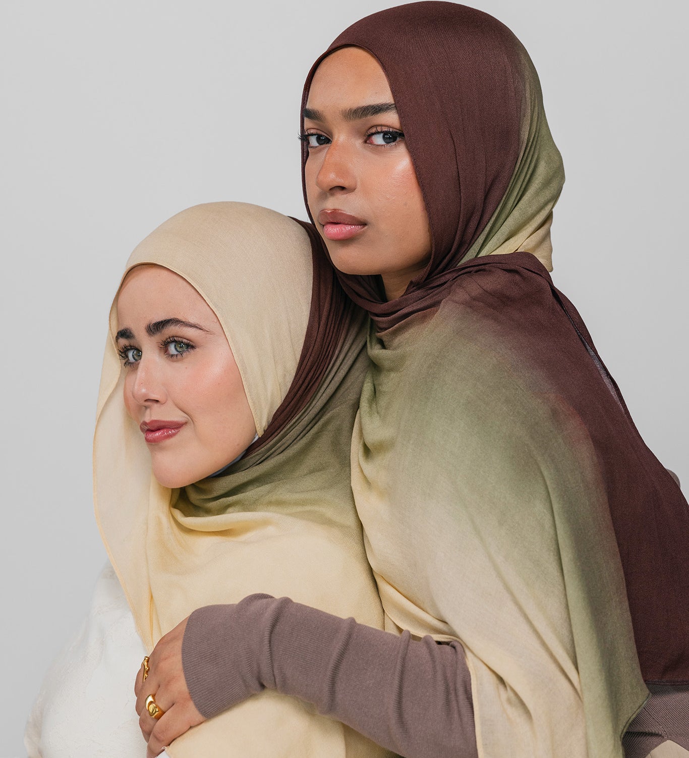 Two women wearing hijabs in beige and brown on a plain background