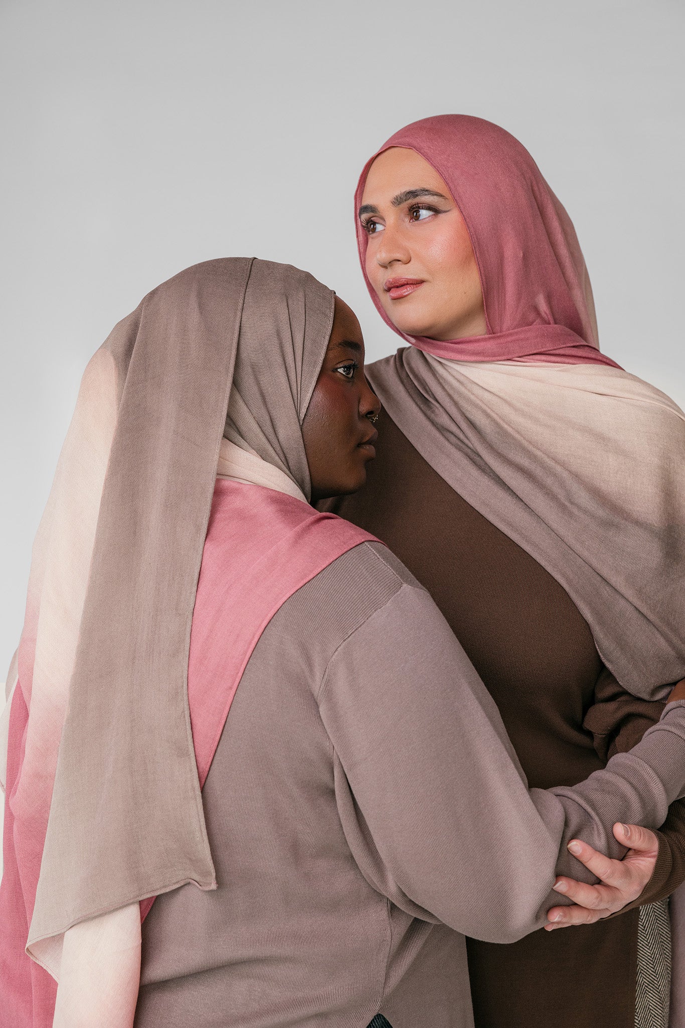 Two women wearing pink and beige ombre hijabs in a neutral setting