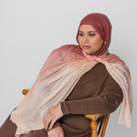 Woman wearing a brown and pink ombre hijab sitting on a wooden chair against a white background
