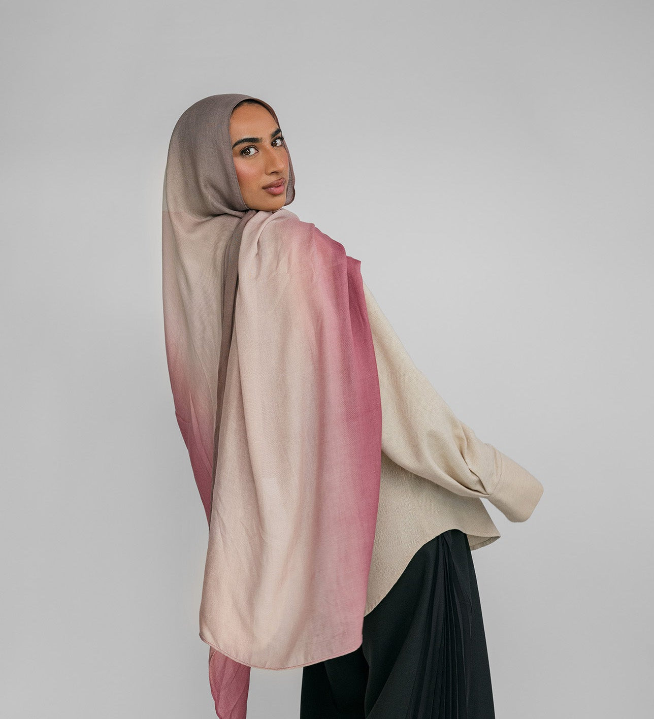 Woman wearing a pink and beige ombre hijab against a plain background