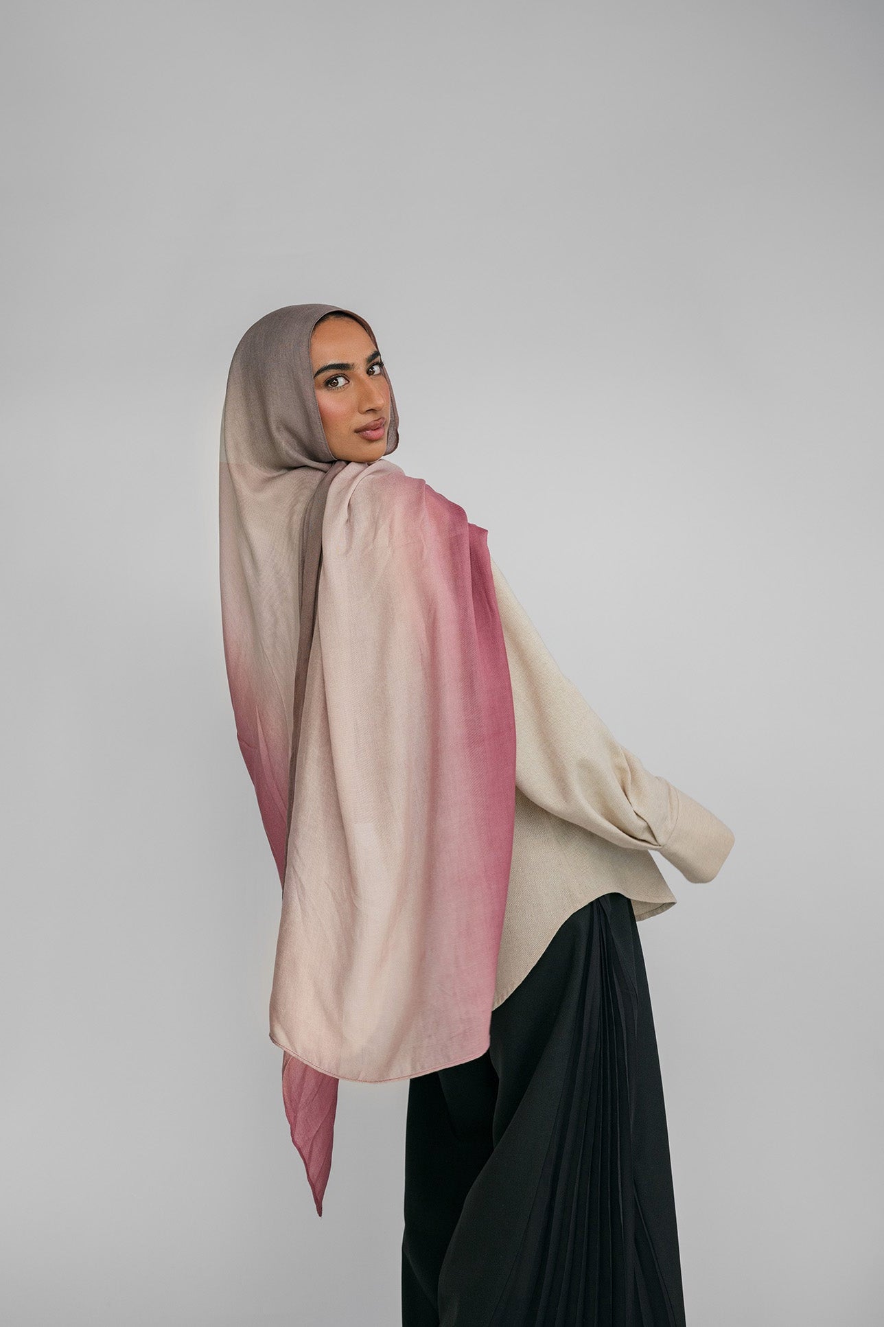 Woman wearing a pink and beige ombre hijab against a plain background