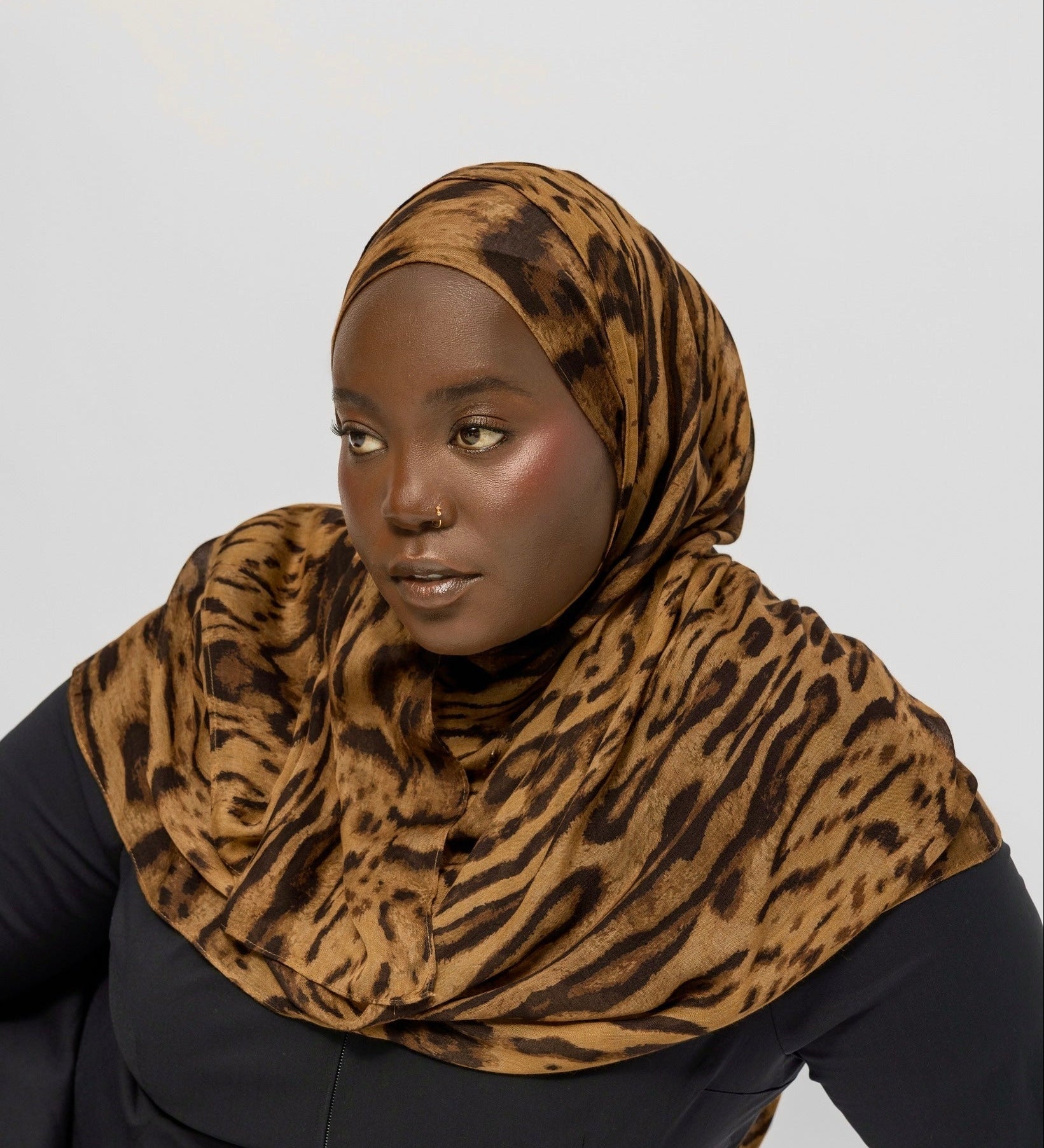 Person wearing a ocelot print hijab and black outfit on a white background