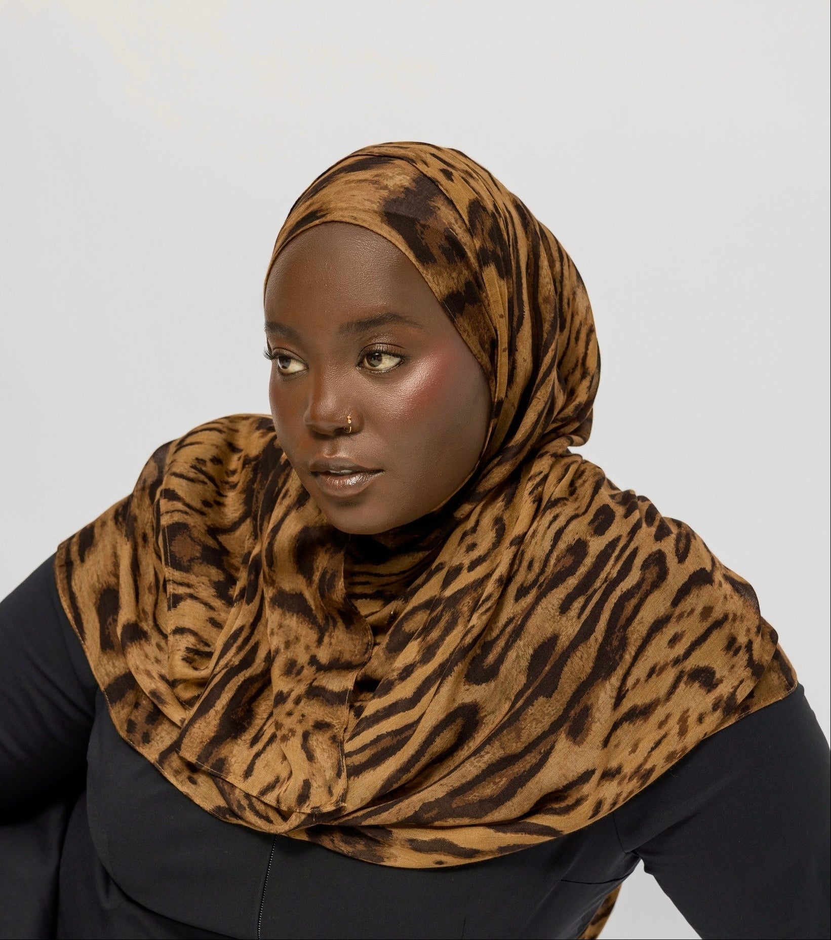 Person wearing a ocelot print hijab and black outfit on a white background