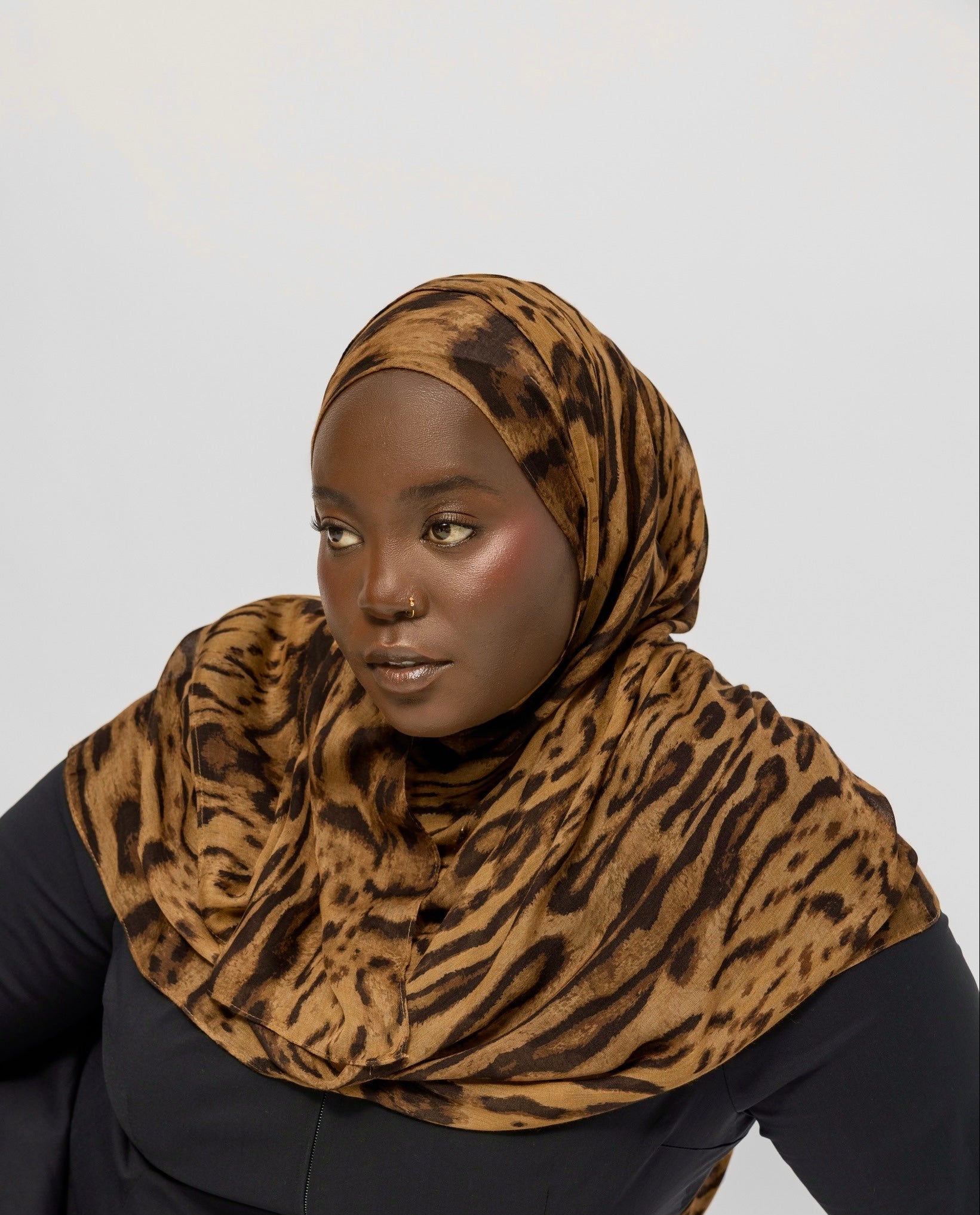 Person wearing a ocelot print hijab and black outfit on a white background