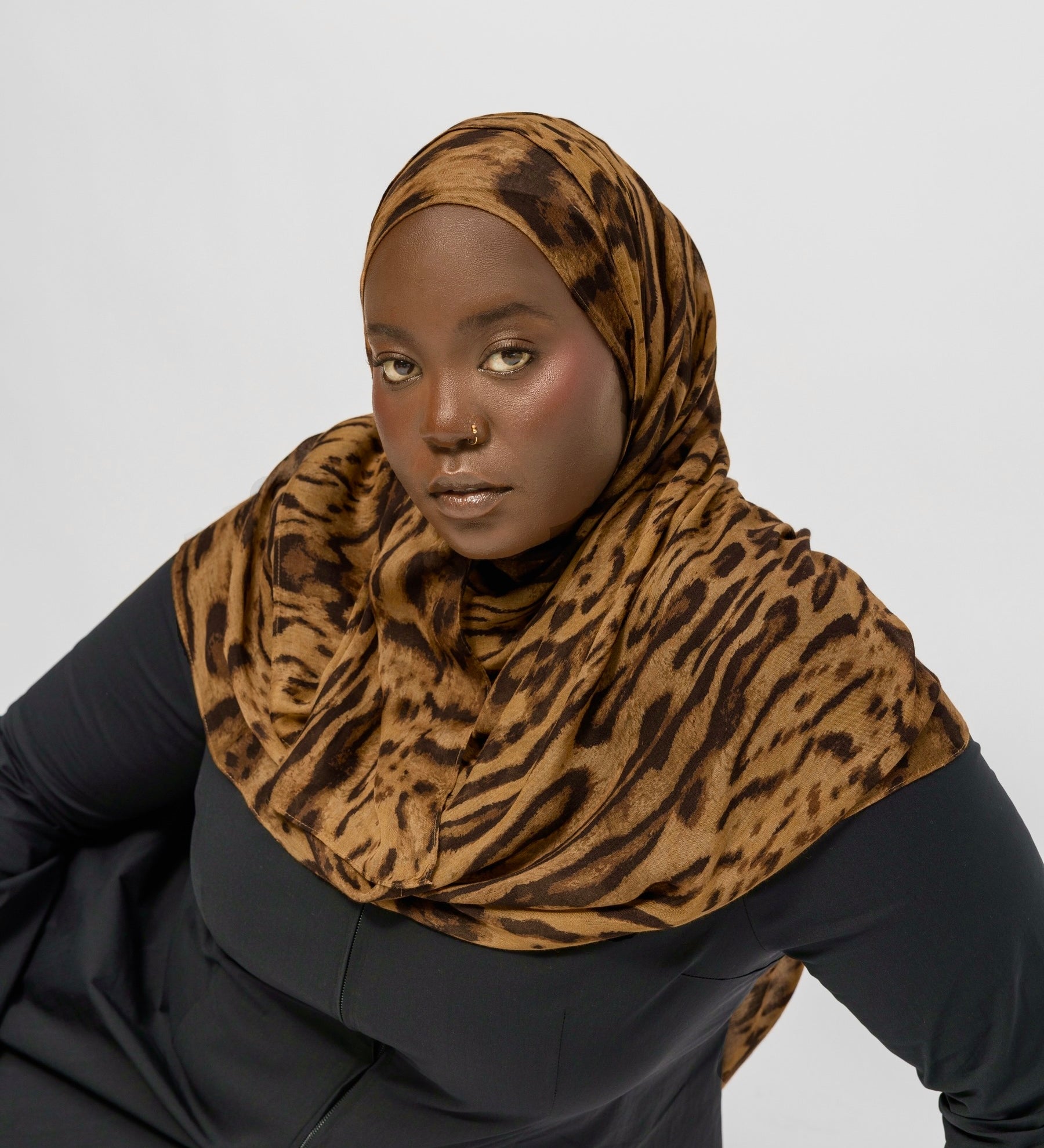 Person wearing a  ocelot print hijab and black outfit on a white background