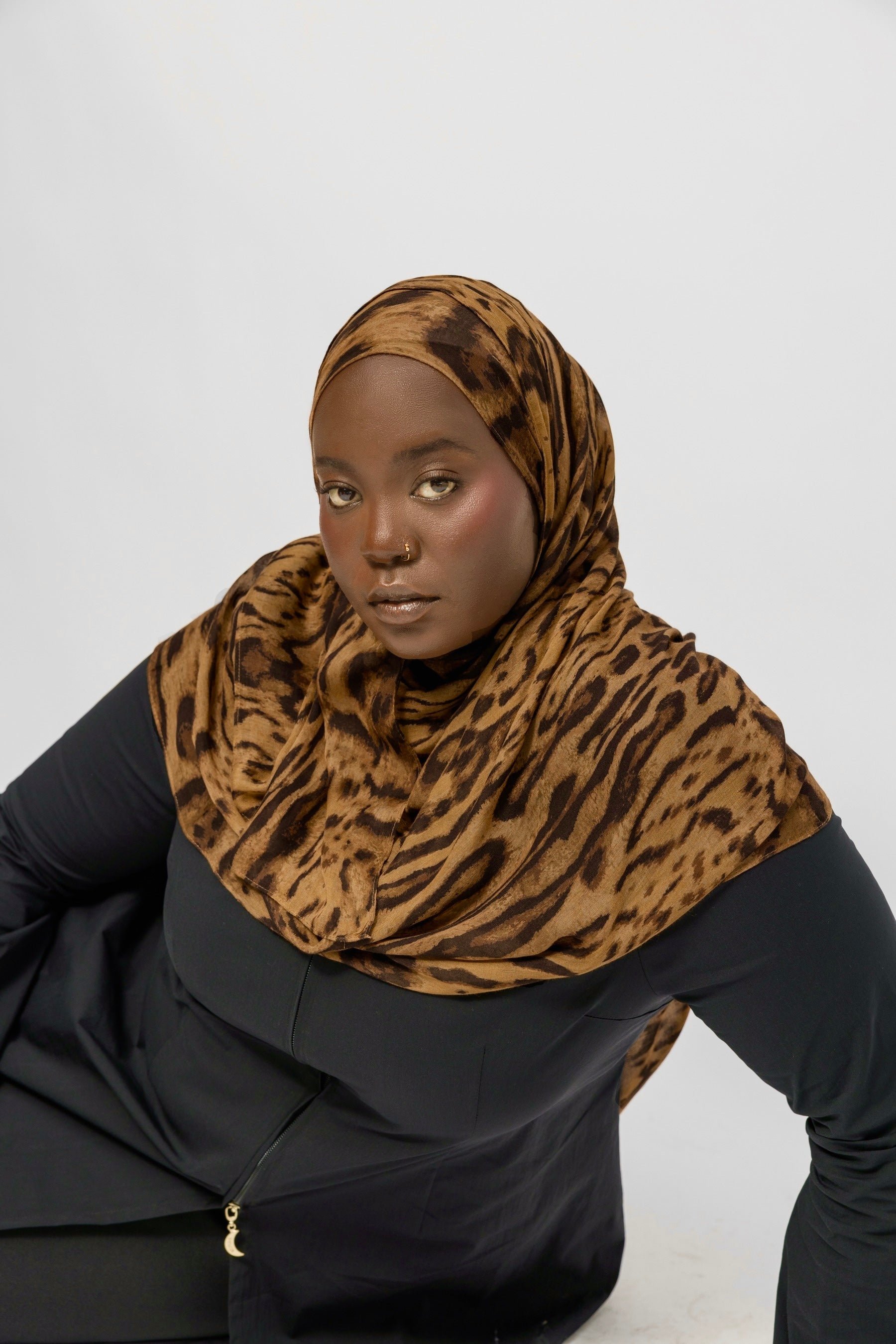 Person wearing a  ocelot print hijab and black outfit on a white background