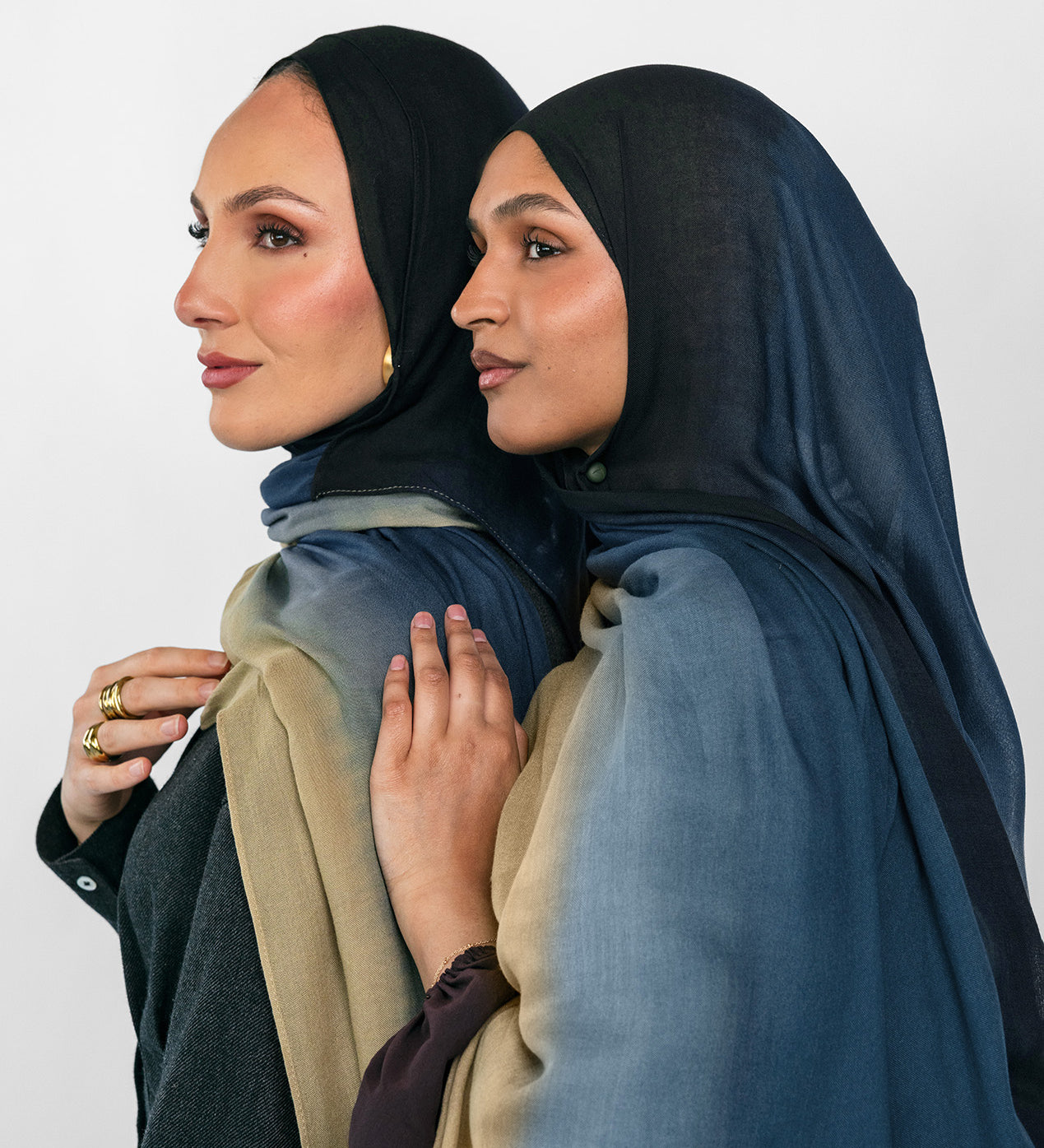 Two women wearing blue ombre hijabs standing close together against a plain background