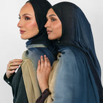 Two women wearing blue ombre hijabs standing close together against a plain background