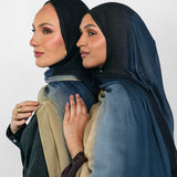 Two women wearing blue ombre hijabs standing close together against a plain background