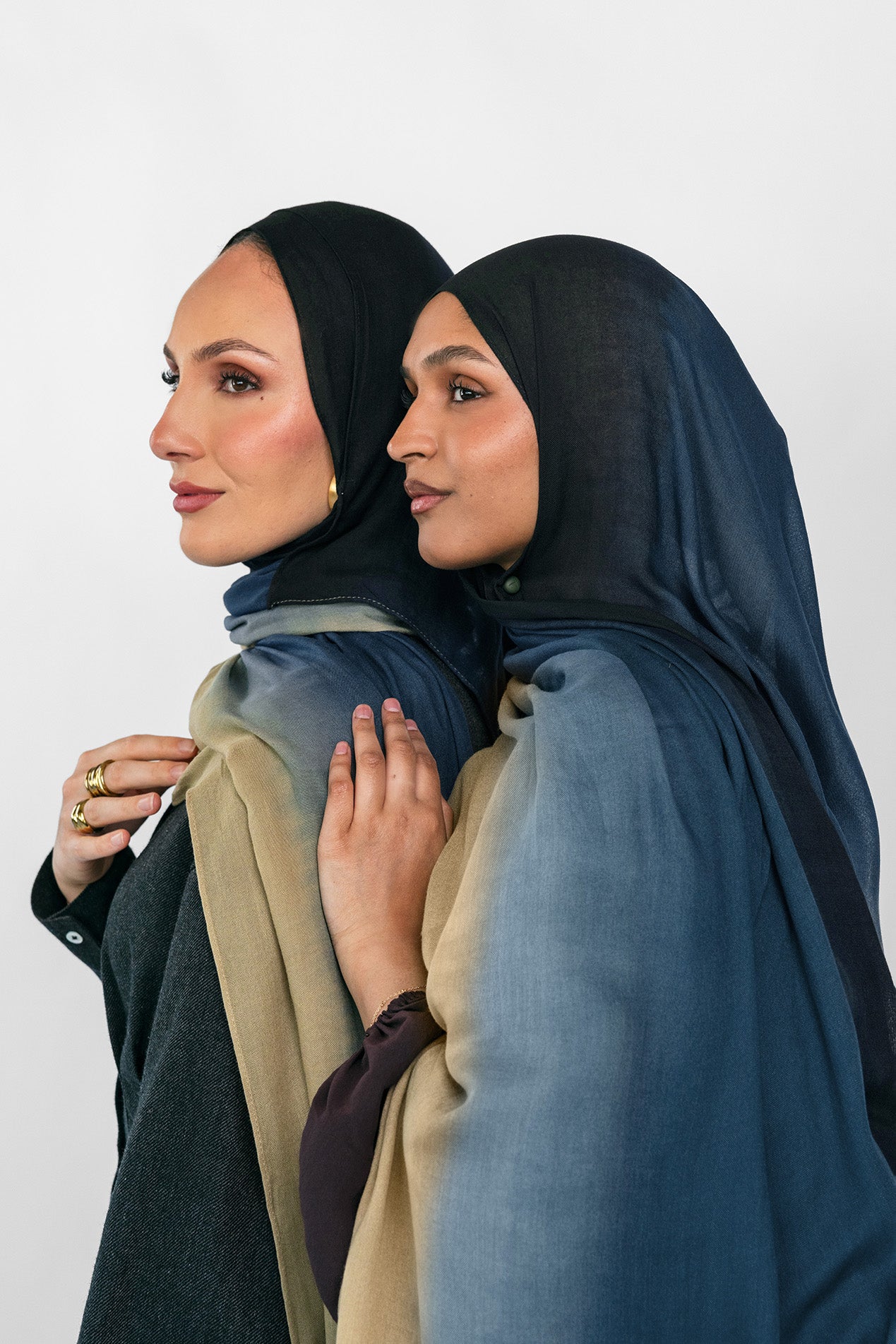 Two women wearing blue ombre hijabs standing close together against a plain background