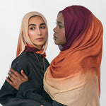 Two women wearing colorful ombre hijabs standing close together against a white background