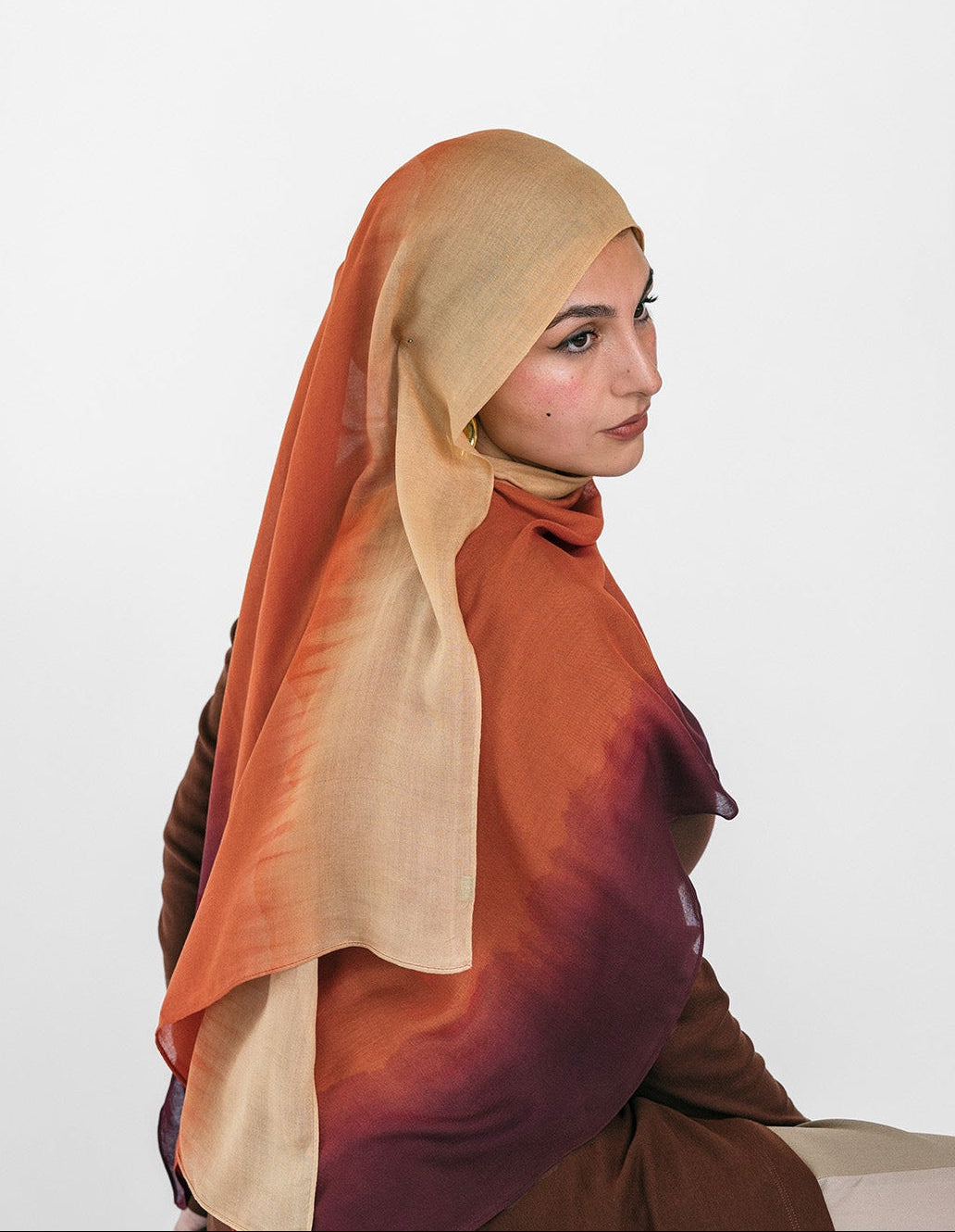 Woman wearing a brown and beige ombre hijab sitting on a white background