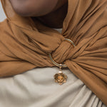 Close-up of a brown hijab with a gold ring and charm, worn by a person.