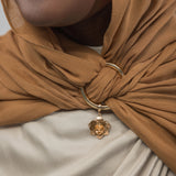 Close-up of a brown hijab with a gold ring and charm, worn by a person.