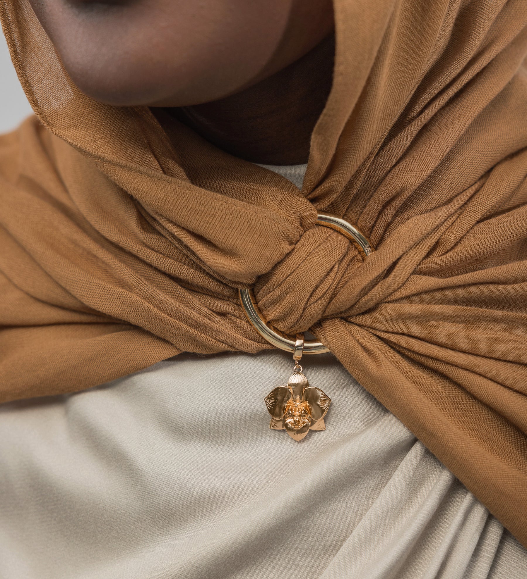 Close-up of a brown hijab with a gold ring and charm, worn by a person.