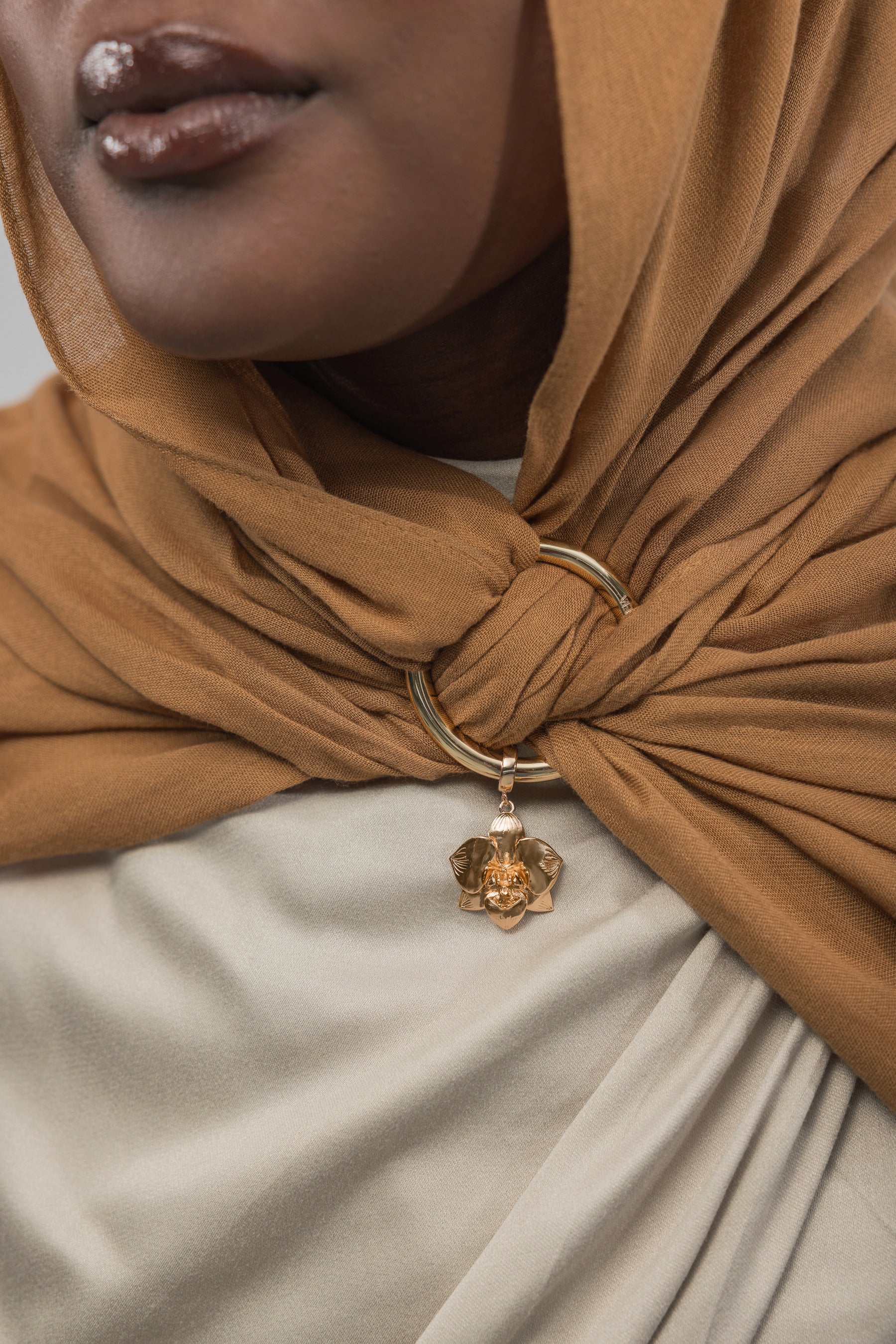 Close-up of a brown hijab with a gold ring and charm, worn by a person.