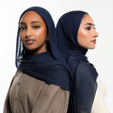 Two women modeling sheer navy blue hijabs, shown from the front and side against a clean white studio background.