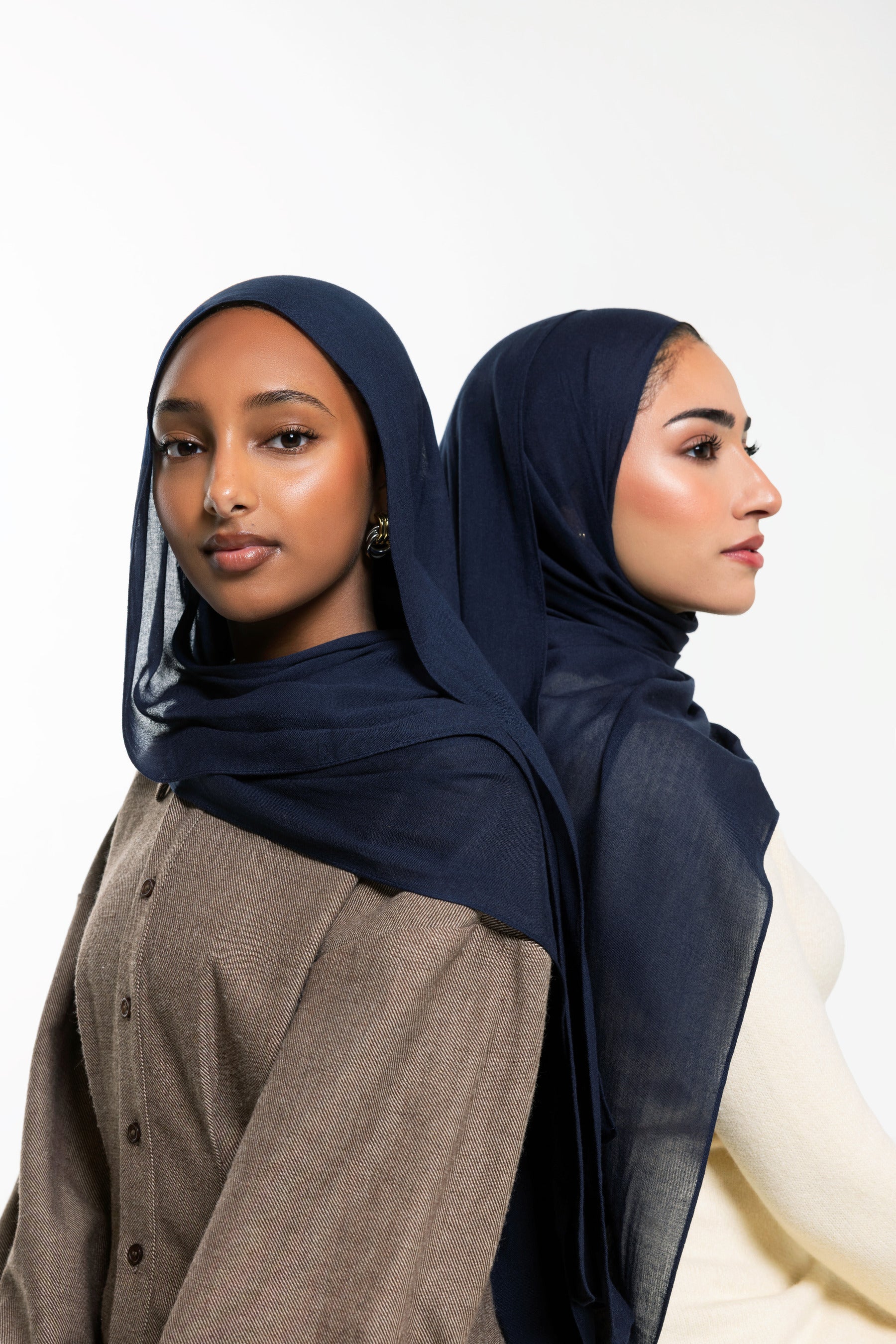 Two women modeling sheer navy blue hijabs, shown from the front and side against a clean white studio background.