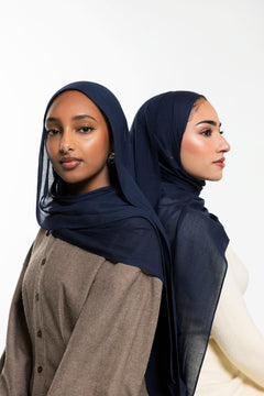 Two women modeling sheer navy blue hijabs, shown from the front and side against a clean white studio background.