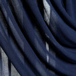 A close-up of draped navy blue sheer fabric with soft folds and light filtering through the material.