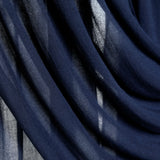 A close-up of draped navy blue sheer fabric with soft folds and light filtering through the material.