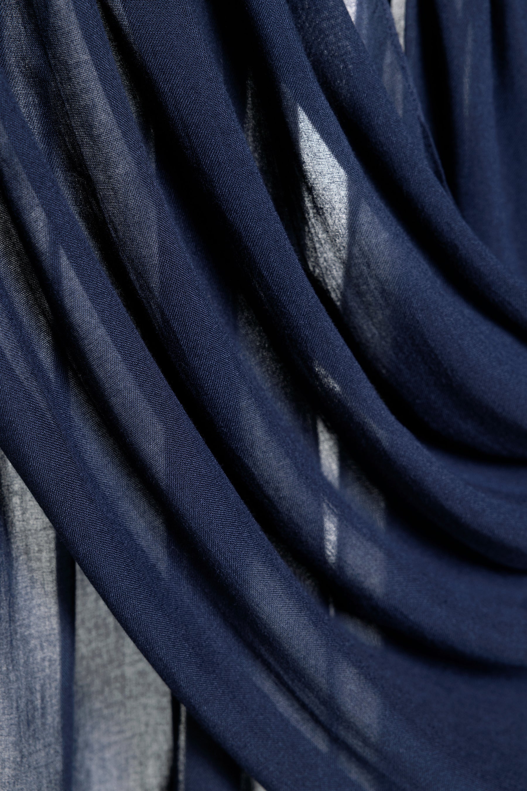A close-up of draped navy blue sheer fabric with soft folds and light filtering through the material.